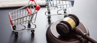 Gavel beside two miniature shopping carts, symbolizing consumer law and retail regulation on a dark surface.
