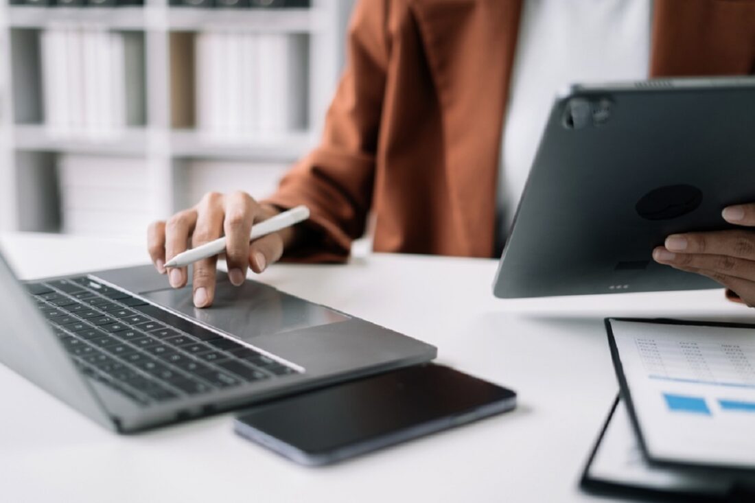 Businesswomen,Using,Tablet,With,Laptop,And,Document,On,Desk,In