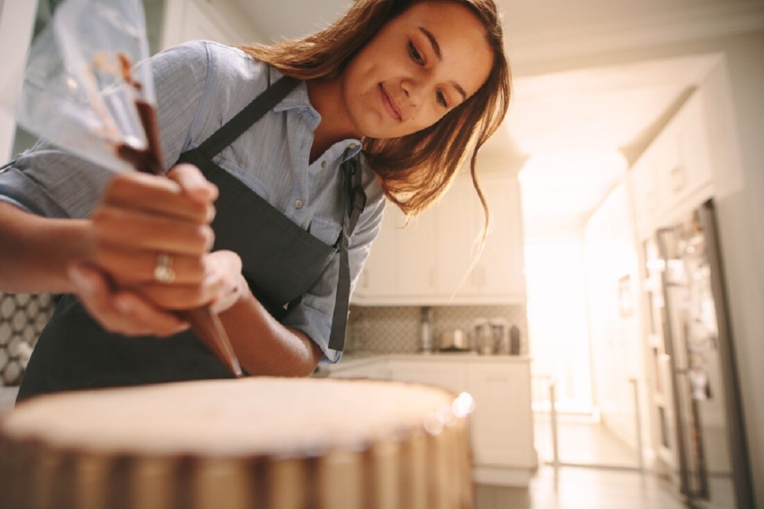 Female,Pastry,Chef,Decorating,A,Cake,With,Chocolate,In,Kitchen.