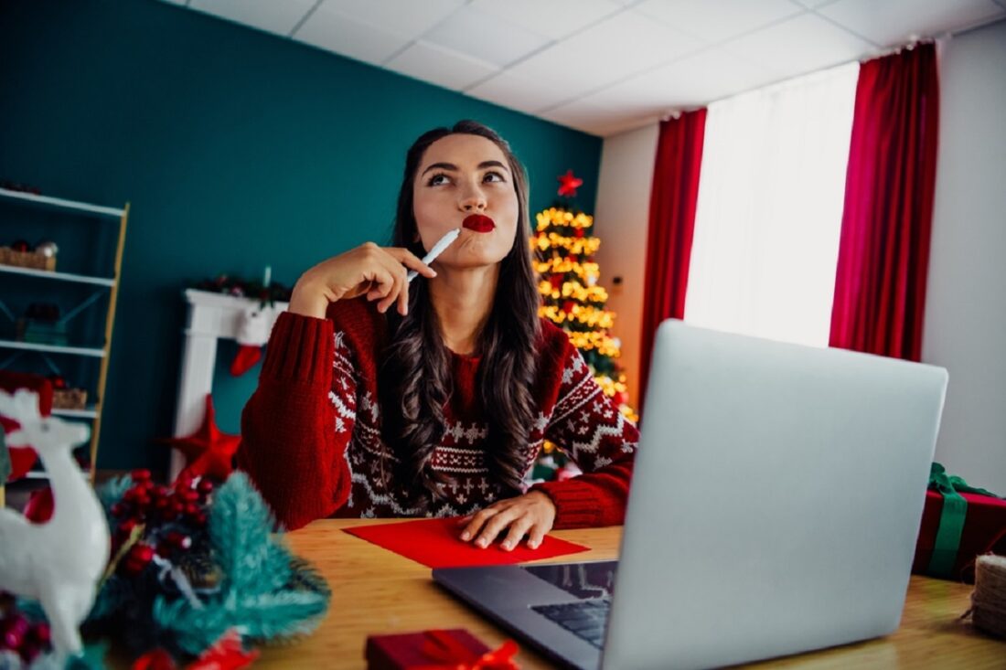 Festive,Young,Woman,Pondering,Holiday,Greetings,At,Desk,With,Laptop