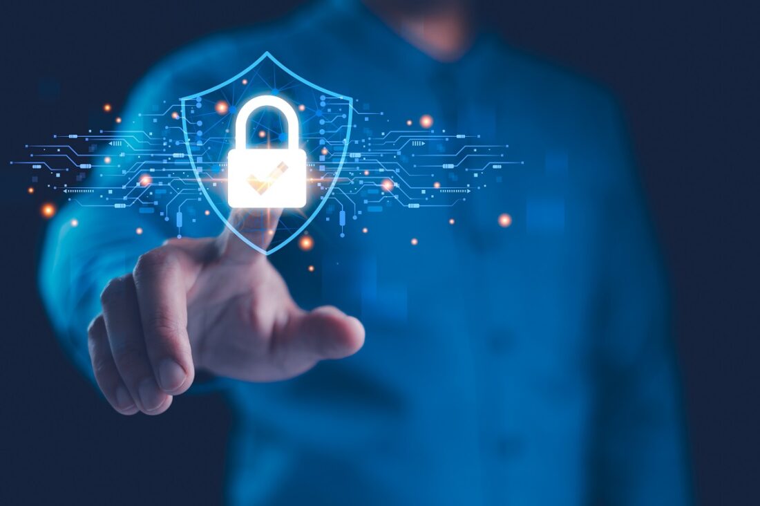 A person in a blue shirt points at a glowing shield with a lock, symbolizing cybersecurity and data protection.