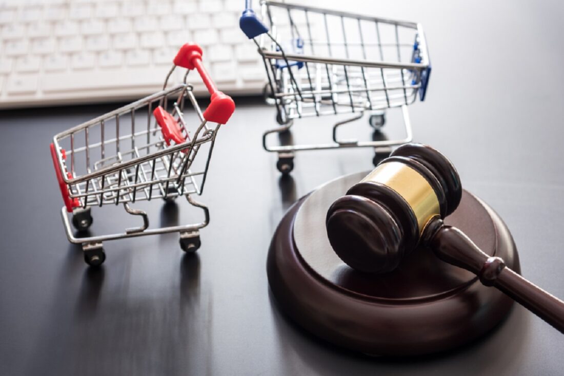 Gavel beside two miniature shopping carts, symbolizing consumer law and retail regulation on a dark surface.